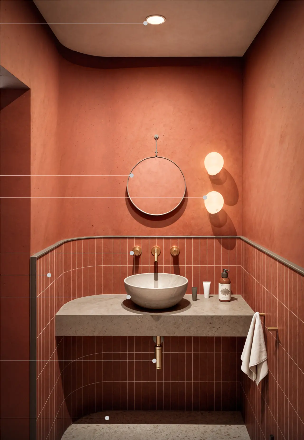 Vedere a băii dormitorului: pereți în tencuială terracotta, lavoar-bol de piatră pe blat masiv, baterie aurie de perete, oglindă rotundă și două aplice globulare.