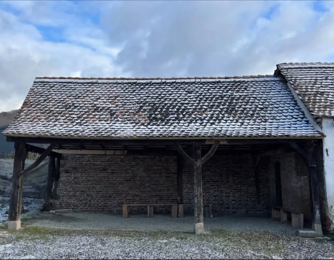 The shed with its pantile roof repaired, under snow, with timber posts and benches beneath the eaves.