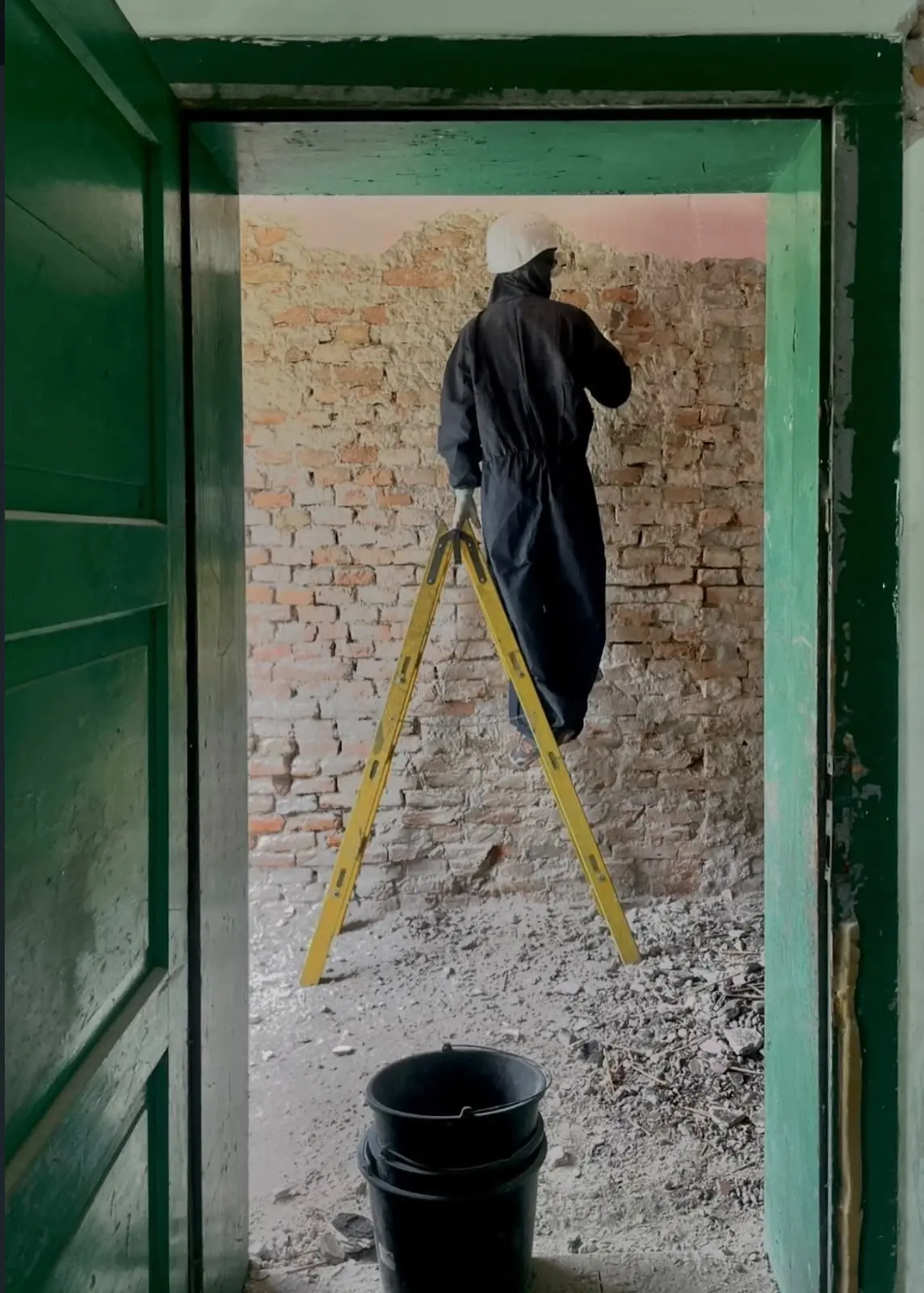 Works stripping render from a brick wall, seen through the green-framed doorway.